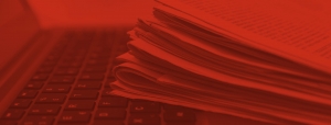 Red-tinted background image of a stack of newspapers on top of a laptop keyboard.