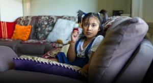Young girl with pigtails sitting on a couch in her living room staring at the camera.