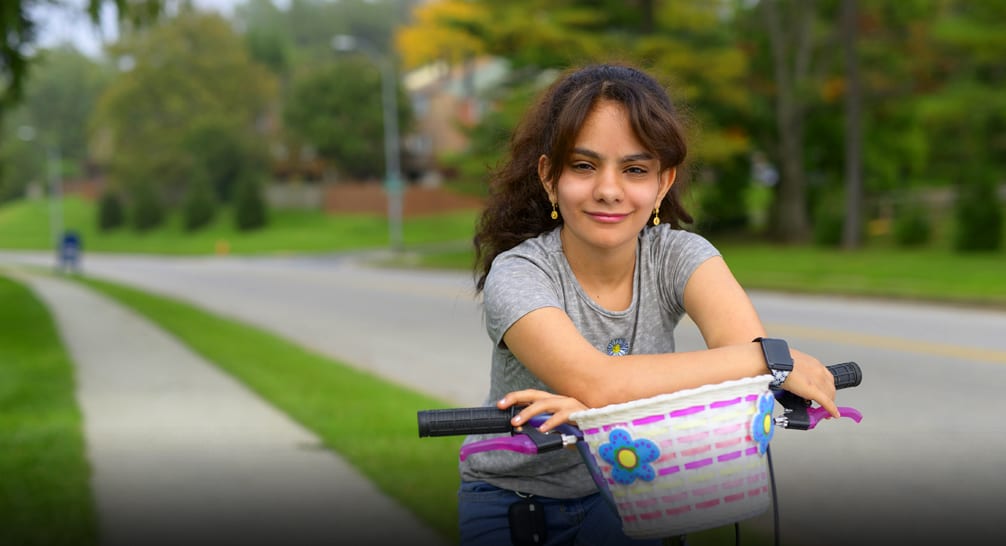Young teenage girl sitting on her bike with arms resting on the handle bars and flowery basket.