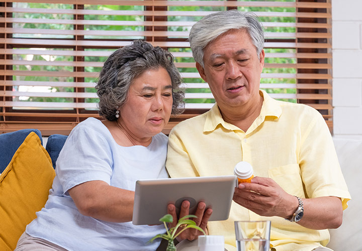 Woman and man looking at tablet while holding a bottle of pills.