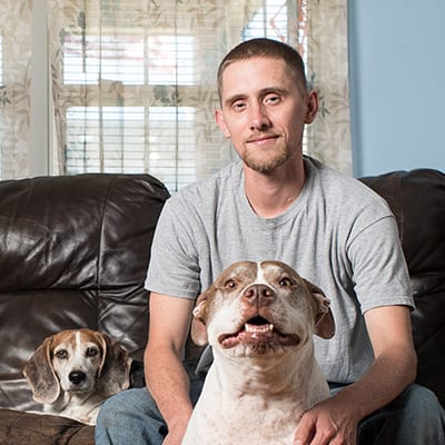 Young adult Caucasian American man sitting on this couch with his two dogs.