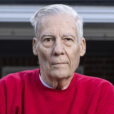 Elderly Caucasian American wearing a red sweatshirt and white hair.